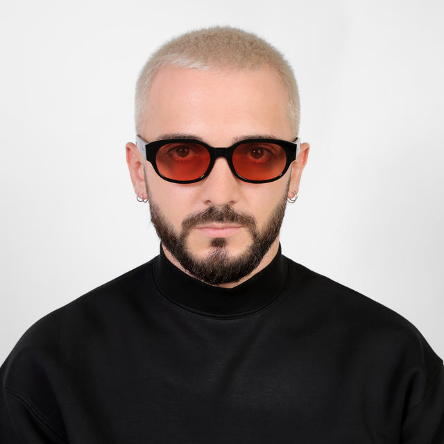 Model with a platinum buzzcut wearing Montreal E Sunglasses Black with Guava See Through