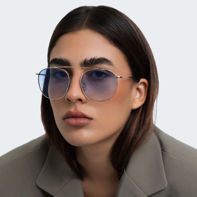 Woman in an oversized gray blazer wearing Mykonos M Sunglasses Gold with Blue Flat Gradient See Through