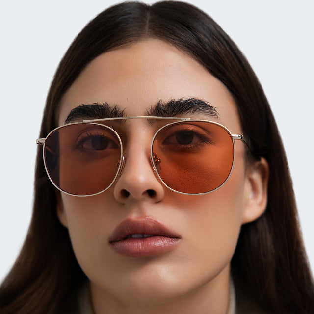 Close up of woman in an oversized gray blazer wearing Mykonos M Sunglasses Gold with Sunset Flat