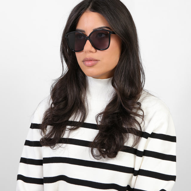 Brunette model in a black and white turtleneck looking right wearing Nancy 57 Sunglasses Black with Grey