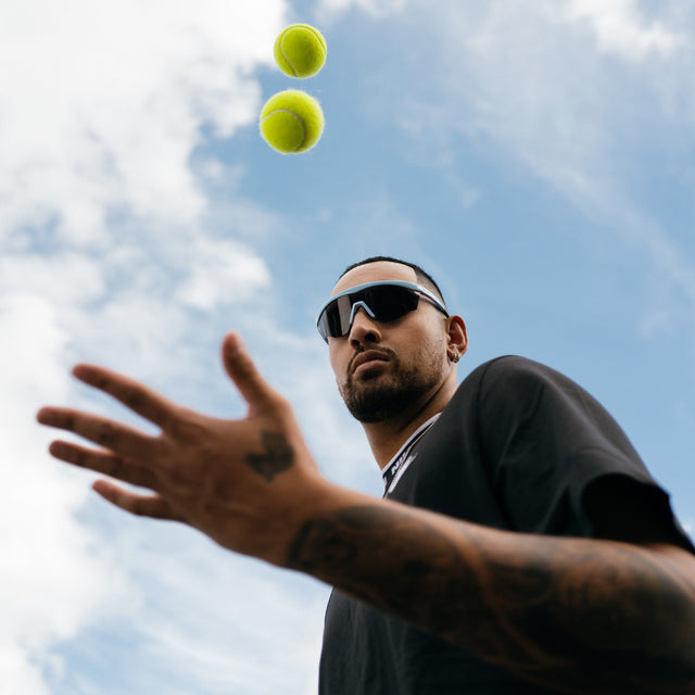 Nick Kyrgios tossing tennis balls wearing Nick Kyrgios x illesteva 1 Sports Frames Baby Blue with Grey