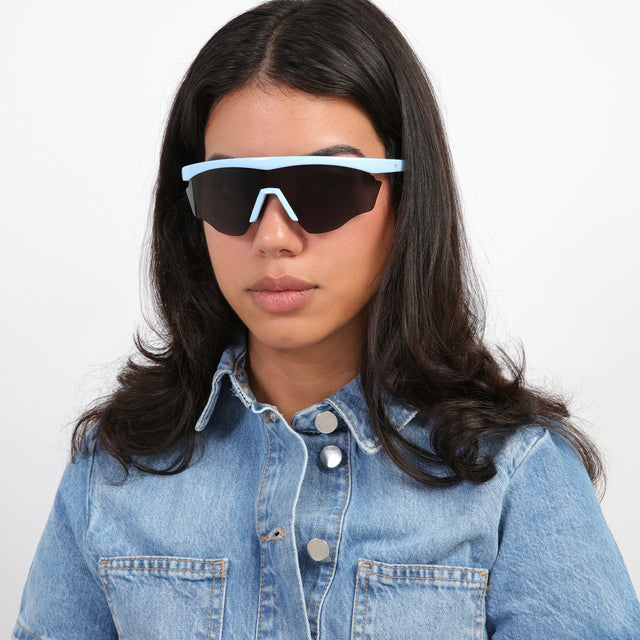 Brunette model in a jean jacket wearing Nick Kyrgios x illesteva 1 Sports Frames Baby Blue with Grey