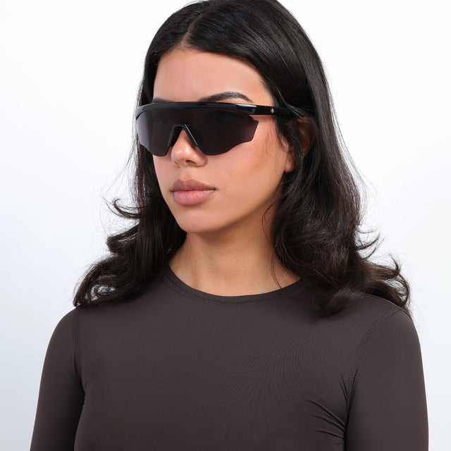 Brunette model with loose curls wearing Nick Kyrgios x illesteva 1 Sports Frames Black with Grey