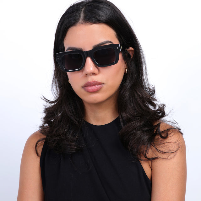 Brunette model with loose curls wearing Nick Kyrgios x illesteva 2 Sunglasses Black with Grey Flat