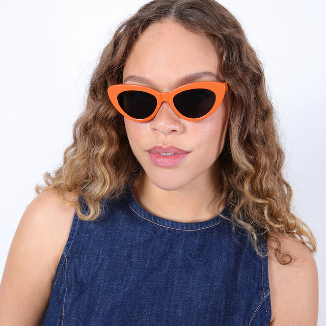 Brunette model with ombré curls wearing Pamela Sunglasses Aperol with Grey Flat