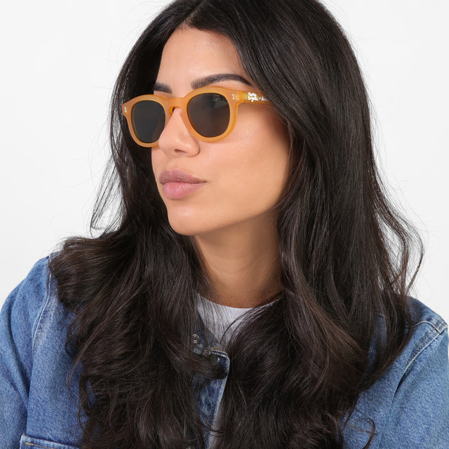 Brunette model looking right wearing PopUp Bagels x illesteva Sunglasses Matte Honey Gold with Olive