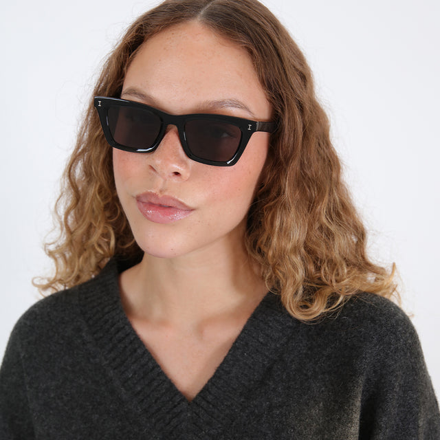 Brunette model with ombré, wavy hair wearing Portugal Sunglasses Black with Grey Flat