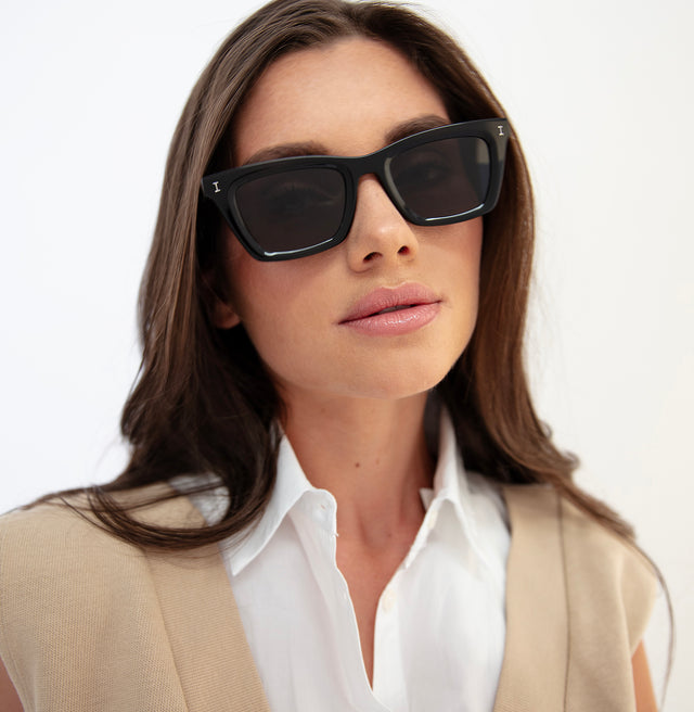 Brunette model with straight hair in a beige vest wearing Portugal Sunglasses Black with Grey Flat