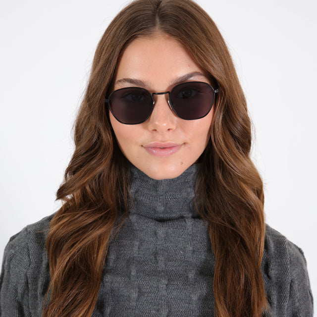 Brunette model with loose curls wearing Prince Sunglasses Matte Black with Grey Flat