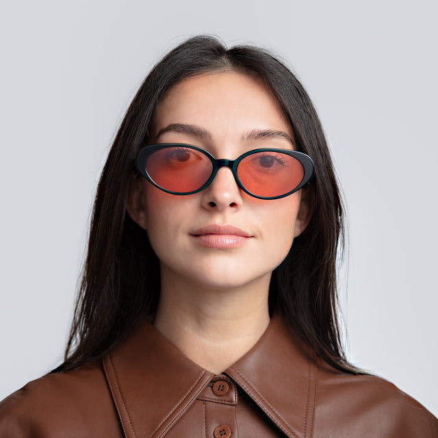Woman in a brown leather blouse wearing Sheila Sunglasses Black with Sunset Flat