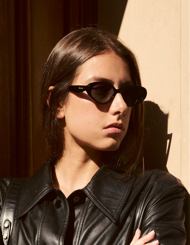 Woman wearing black Sheila sunglasses and a black jacket in Paris