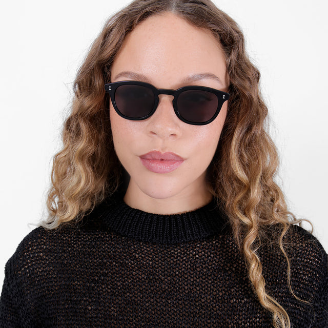 Brunette model with ombré, nature curls wearing Slope Sunglasses Black with Grey