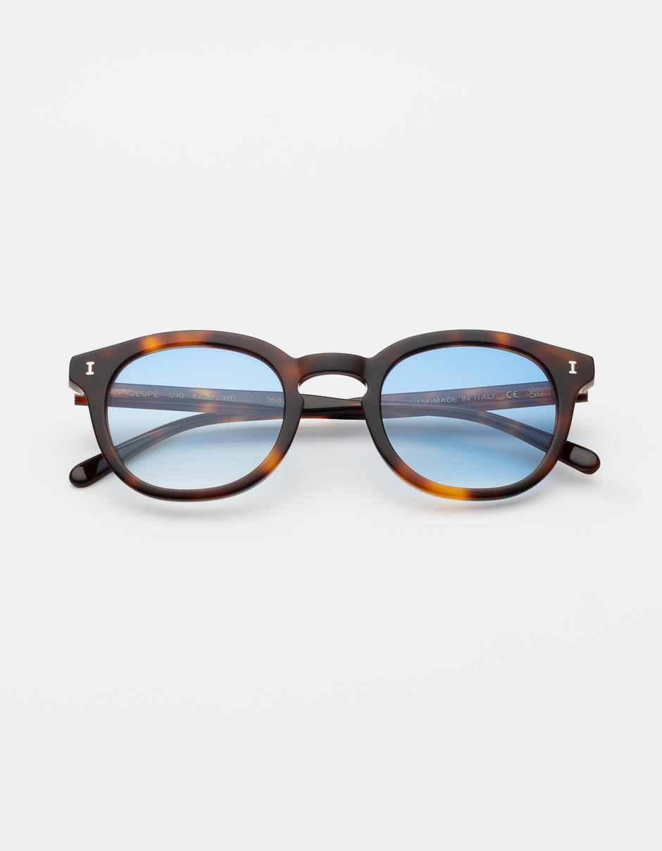 The Slope Sunglasses in Havana with Blue See Through lenses on a grey counter