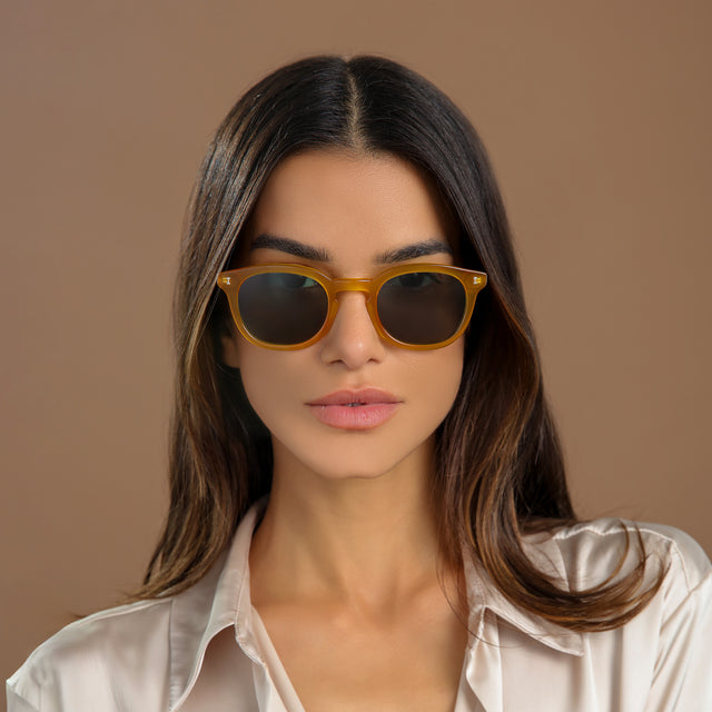 Brunette woman in a cream silk blouse wearing Slope Sunglasses Honey Gold with Olive