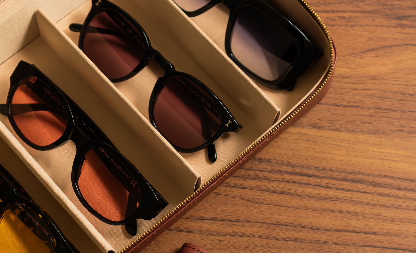 Two pairs of sunglasses in a collector's case on a wooden surface