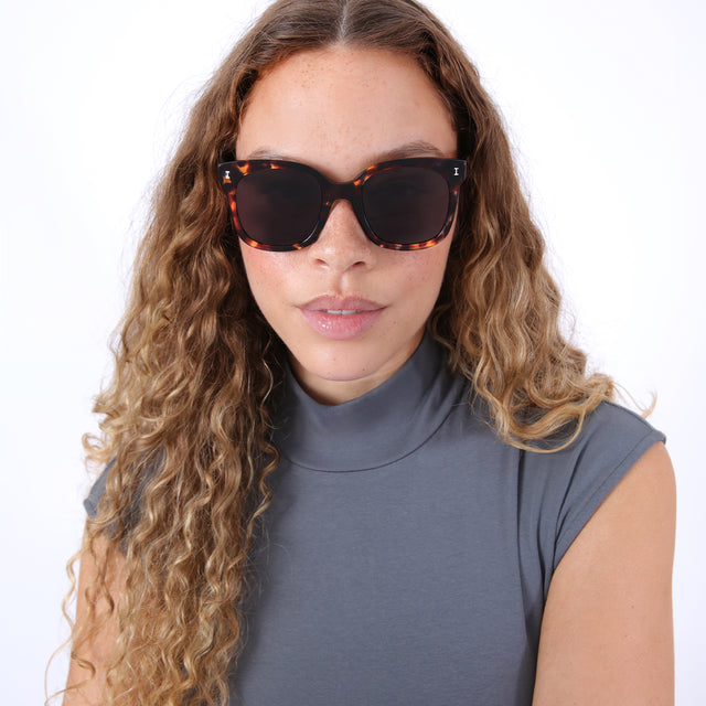 Brunette model with ombré, natural curls wearing Valencia Sunglasses Sea Glass with Grey