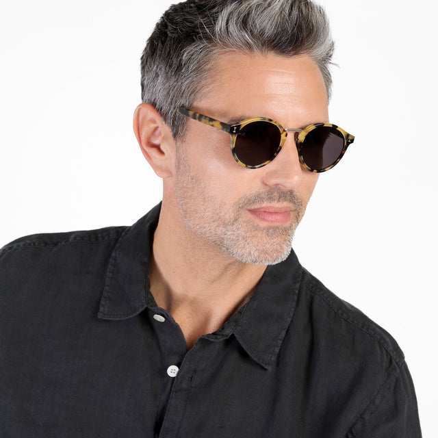 Model with salt and pepper hair and beard looking left wearing Village Sunglasses Tortoise/Gold with Grey