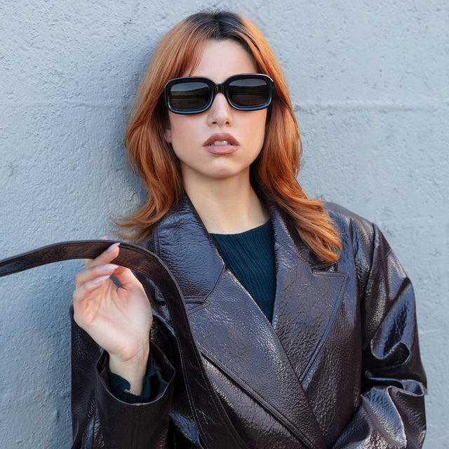 Model in a leather jacket holding her leather belt wearing Vinyl Sunglasses Black with Grey