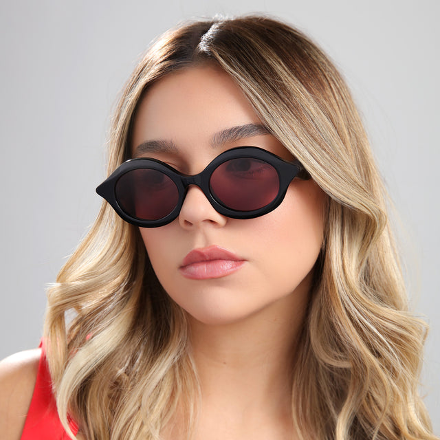 Blond woman in a red blouse wearing Willow Sunglasses Black with Plum See Through