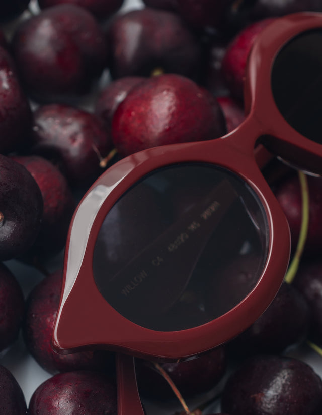 The Willow sunglasses in Bordeaux with dark lenses on a background of cherries