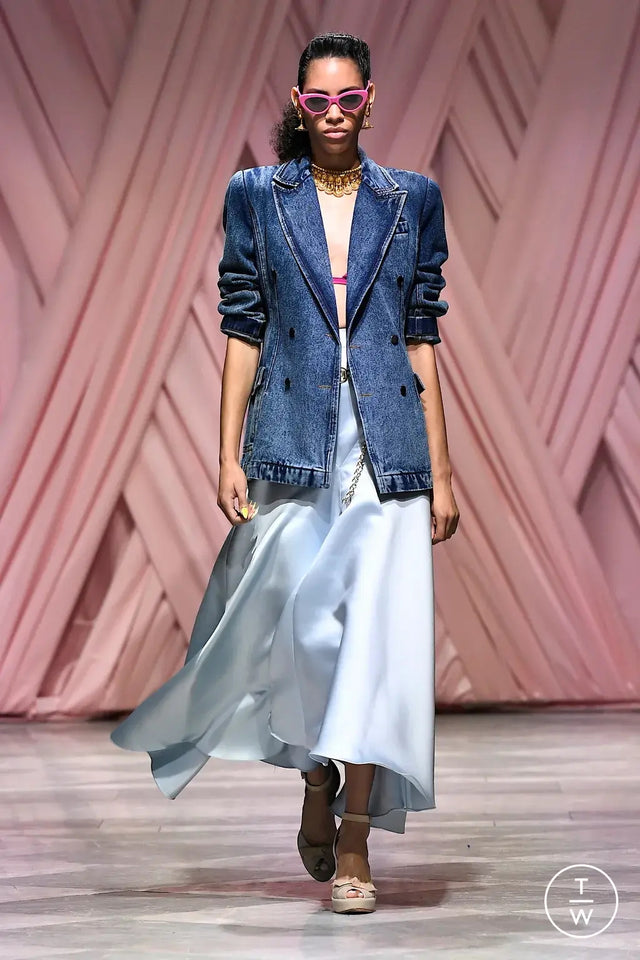 Model walking on a runway wearing a denim jacket, a light blue skirt, and the Pamela Sunglasses