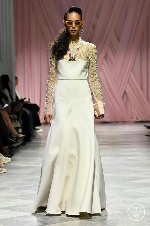 Model wearing a long, elegant dress with a lace top and satin skirt on a runway.