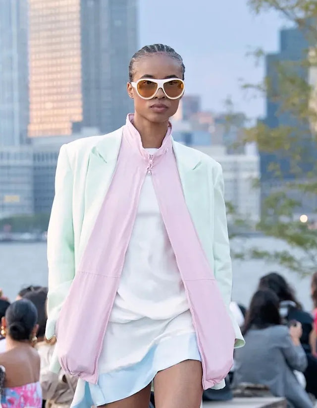 Woman wearing Cynthia Rowley x illesteva  and a pastel green jacket with a pink scarf on the runway