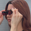 Model with red hair in front of a gray brick wall wearing the Encinitas Sunglasses in Black with Plum See Through