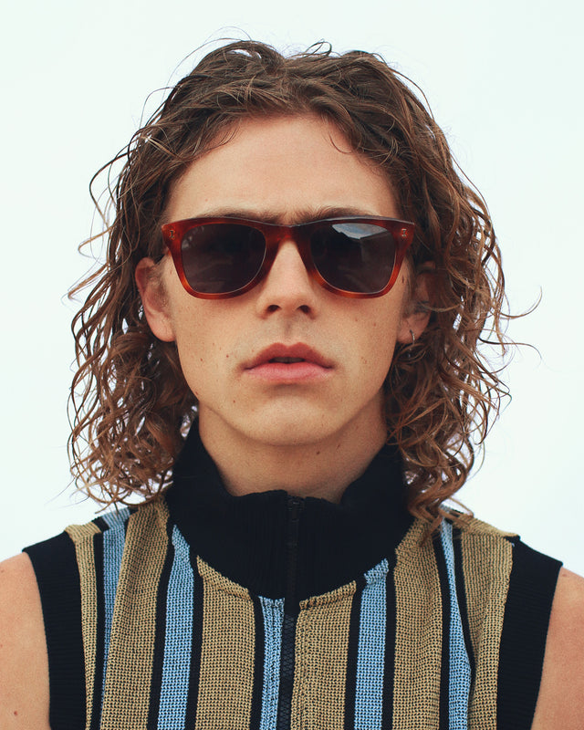 Model with medium wavy hair in a striped zip-up wearing Austin Sunglasses Red Havana with Grey Flat