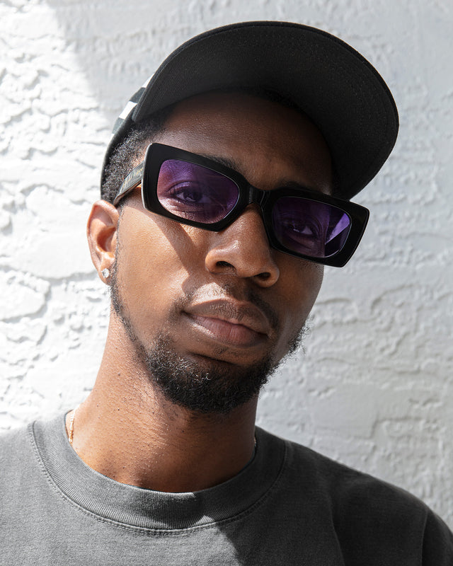 Bearded model in a baseball cap wearing Field Trip x illesteva Sunglasses Black with Purple Flat Gradient