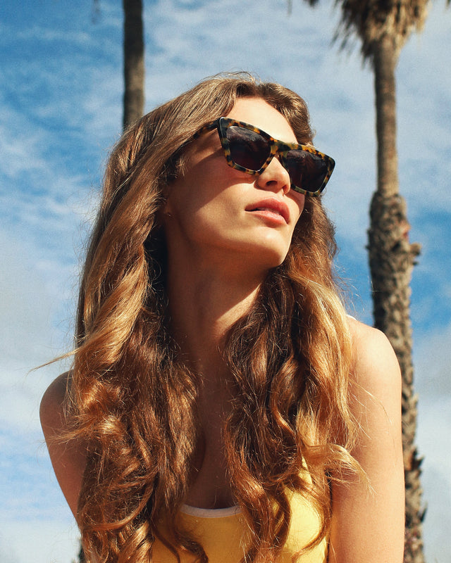 Brunette model near palm trees wearing Lisbon Sunglasses Tortoise with Grey