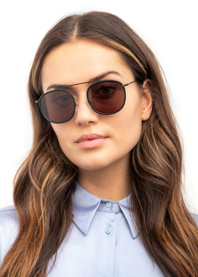 Brunette model with wavy hair wearing Mykonos Ace Sunglasses Matte Black with Grey Flat