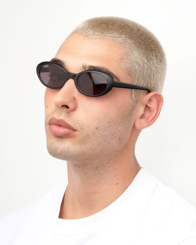 Angled pose of model with blonde buzzcut wearing Seattle Sunglasses Matte Black with Grey Flat Lenses